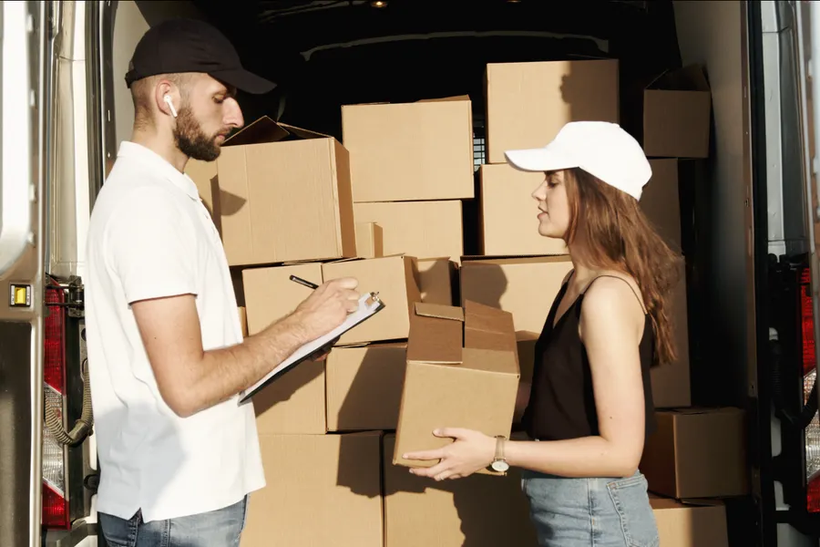 Repartidor entregándole cajas a una clienta junto a la camioneta de reparto